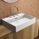 Weißer Waschtisch von Ideal Standard mit zwei Wasserhahnöffnungen und moderner, rechteckiger Form. Montiert auf einer Holzfläche, hinter einer korkartigen Wand.